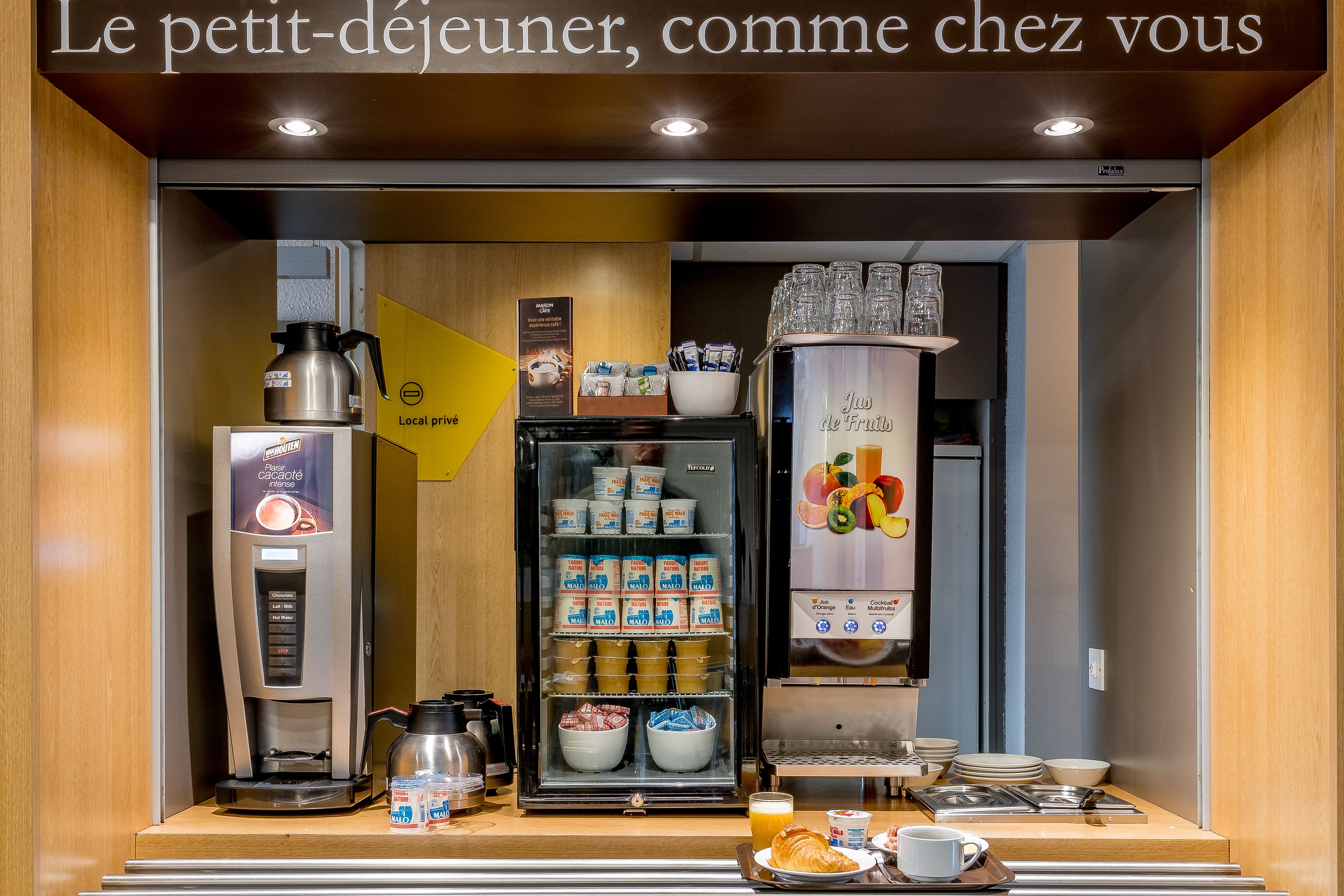 Un espace réservé au petit-déjeuner, équipé d’une machine à café, de boissons fraîches et d’un présentoir de fruits.