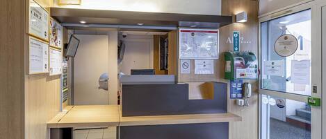 A reception desk with a wooden counter, a glass door entrance, and various informational posters and signs.
