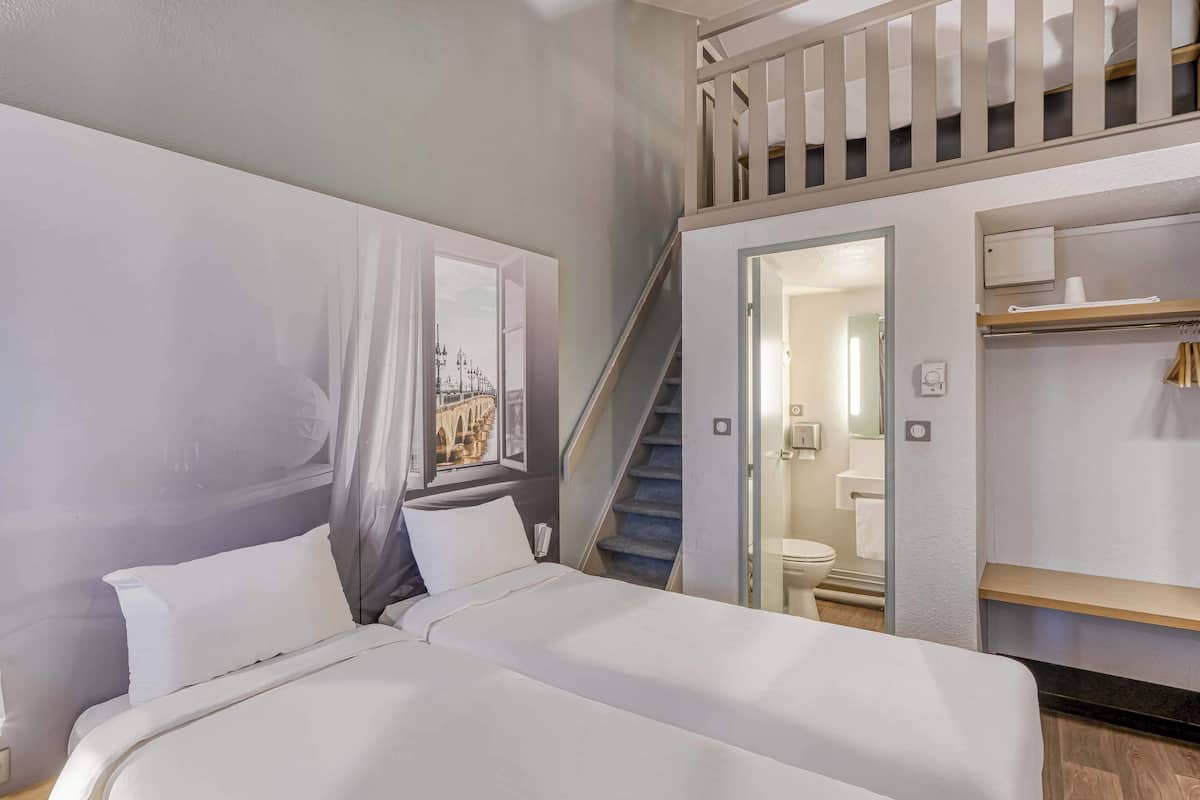 Quarto de hotel com cama, escada, banheiro e vista para a paisagem urbana.