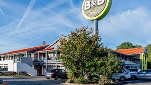 Un hotel B&B con un letrero llamativo, un edificio de techo rojo y un estacionamiento con coches.