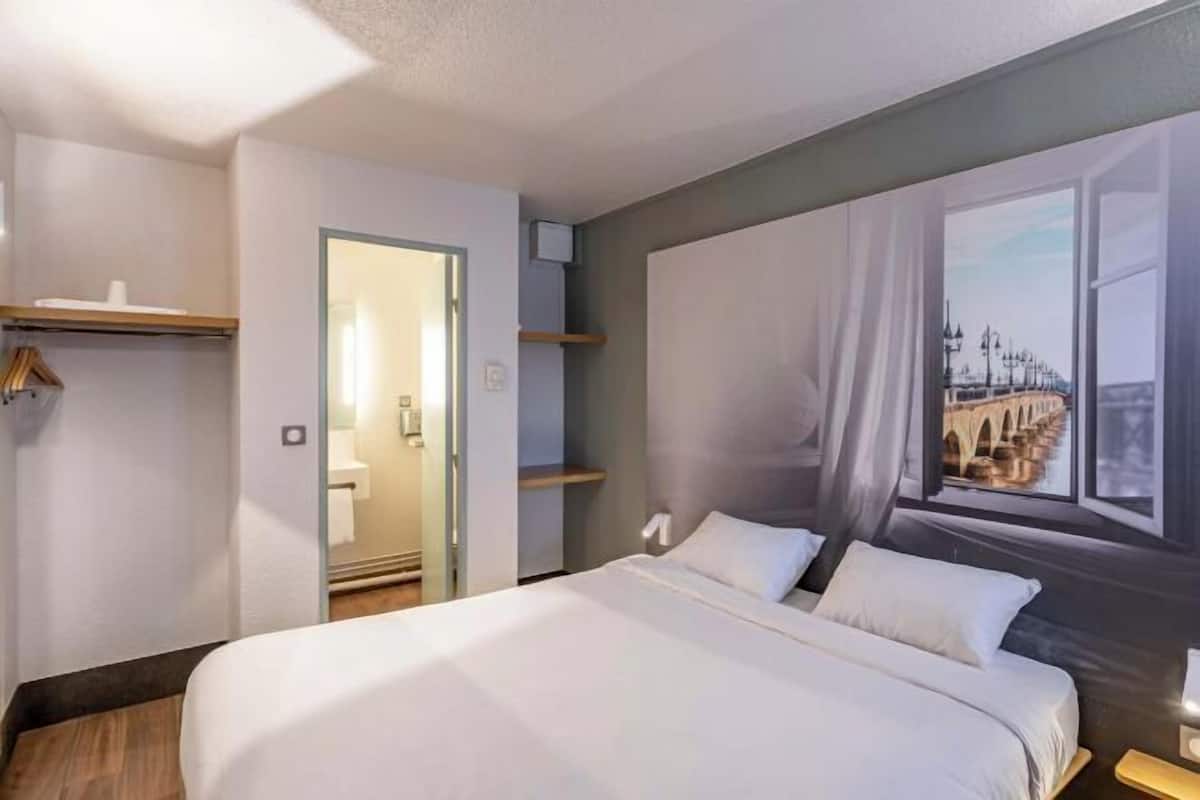 Quarto de hotel com cama, janela com vista, porta e espelho.