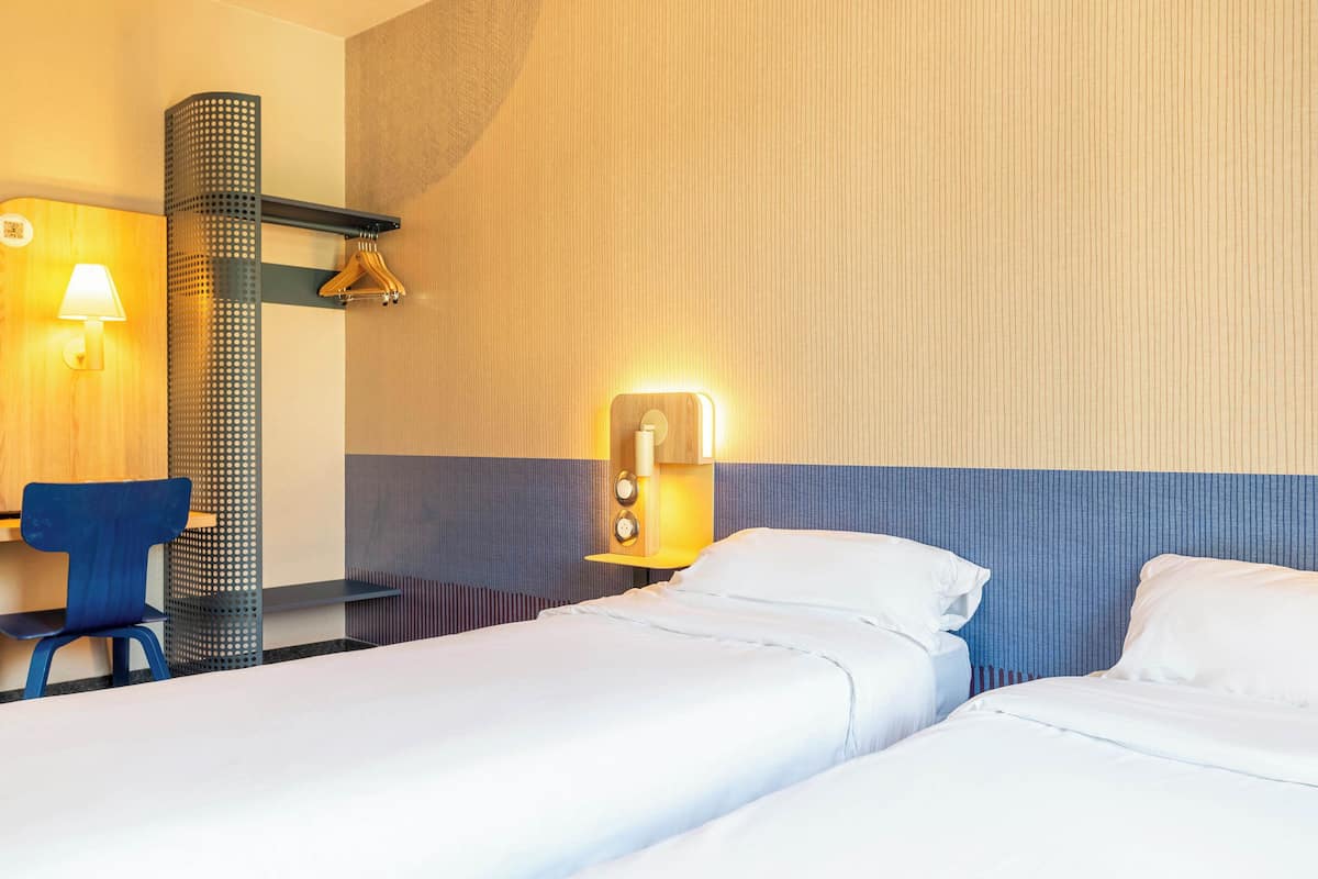 Habitación de hotel con dos camas, un escritorio y una silla. Hay lámparas de pared y una lámpara colgante.