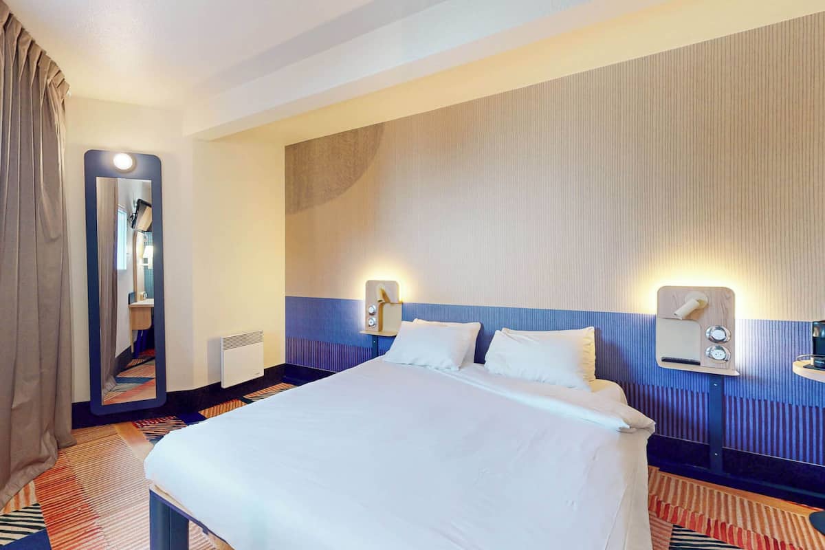 Habitación de hotel con una cama grande, un espejo, dos mesitas de noche con lámparas y una alfombra estampada.