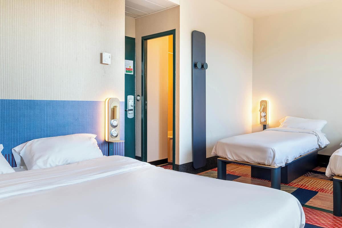 Una habitación de hotel con dos camas, una puerta, una lámpara fijada a la pared y una mesita.