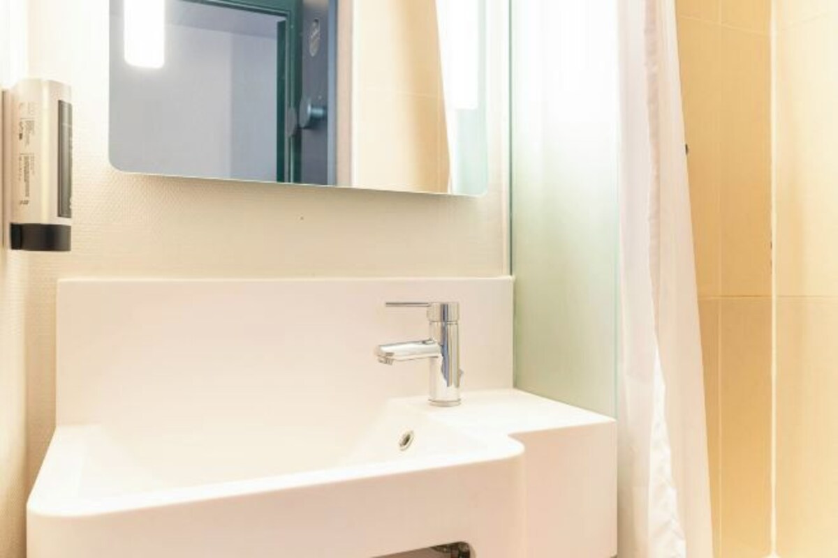 Een badkamer met een witte wastafel, een spiegel erboven en een douchegordijn.