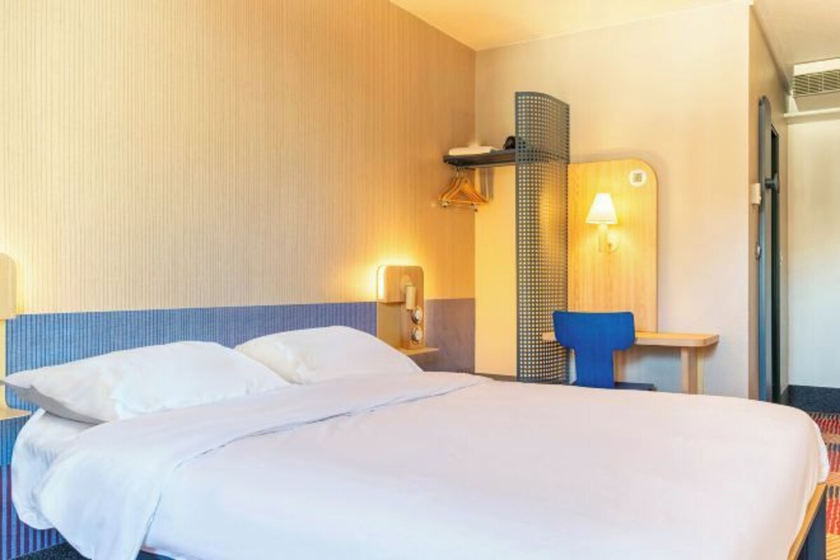 Hotelkamer met een groot bed, een bureau met stoel, een wandlamp en een klein plankje met een handdoek.