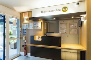 A reception desk with a sign reading 'Bienvenue chez B&B' and various informational posters. - B-B Hotel Nantes Parc Expos LA Beau (Nantes)