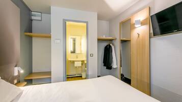 A hotel room with a bed, a TV, a wardrobe, a mirror, and a bathroom visible through an open door.