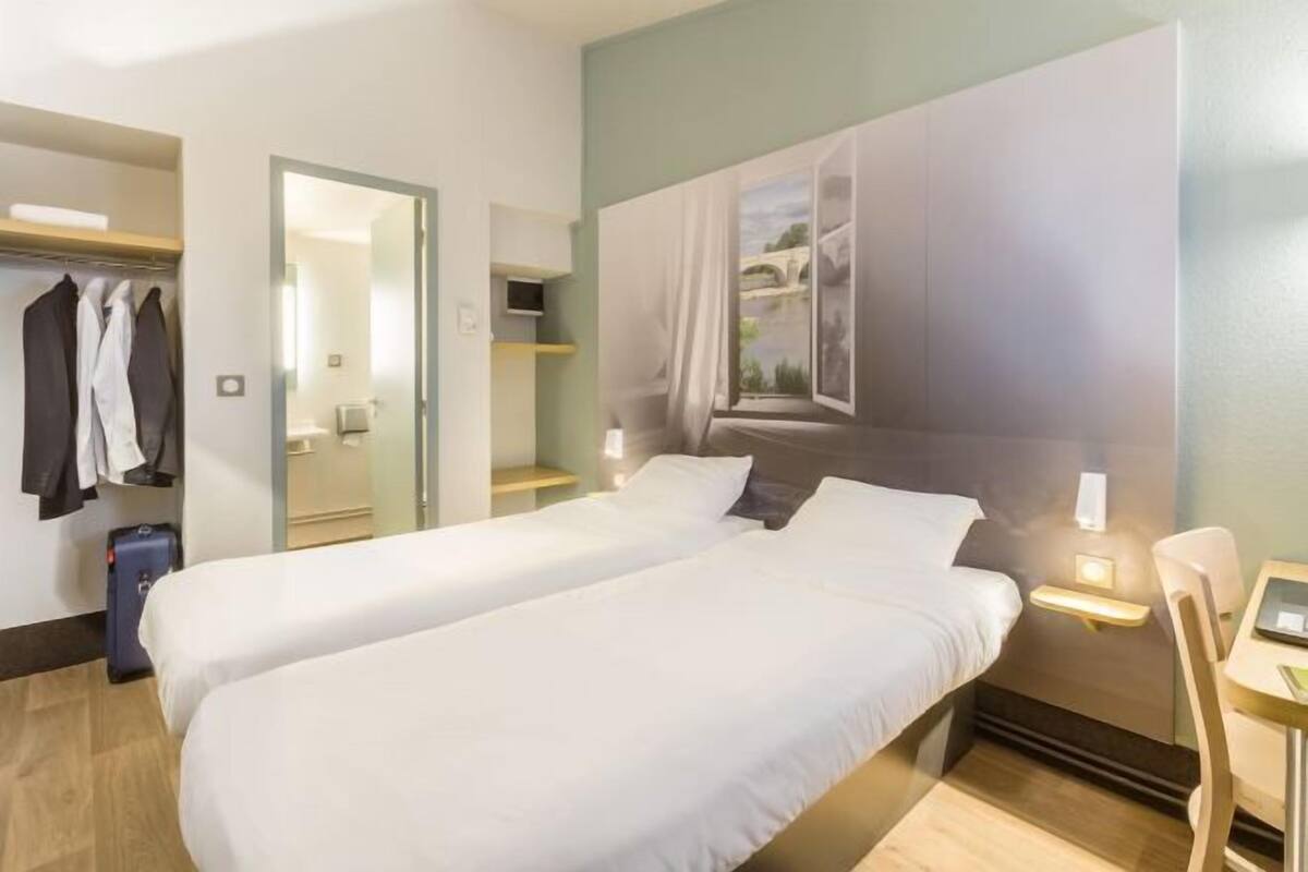 Ein Hotelzimmer mit zwei Betten, einem Schreibtisch, einem Stuhl, einem Kleiderschrank und einem Spiegel.