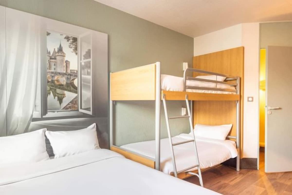 Una habitación con literas, una cama, un cuadro de un castillo y una puerta.