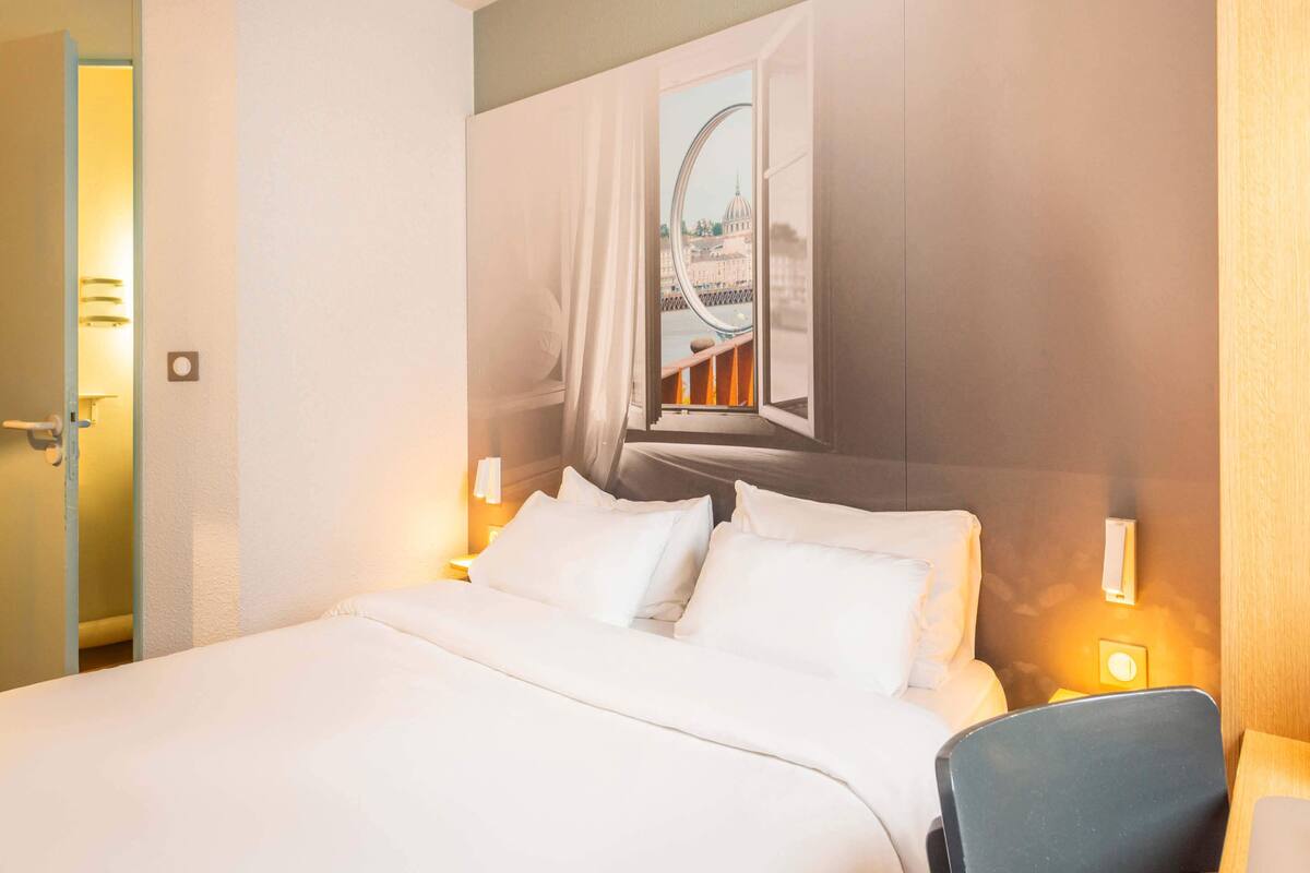 Ein Hotelzimmer mit Bett, Stuhl und Fenster mit Blick auf eine Brücke und ein Gebäude.