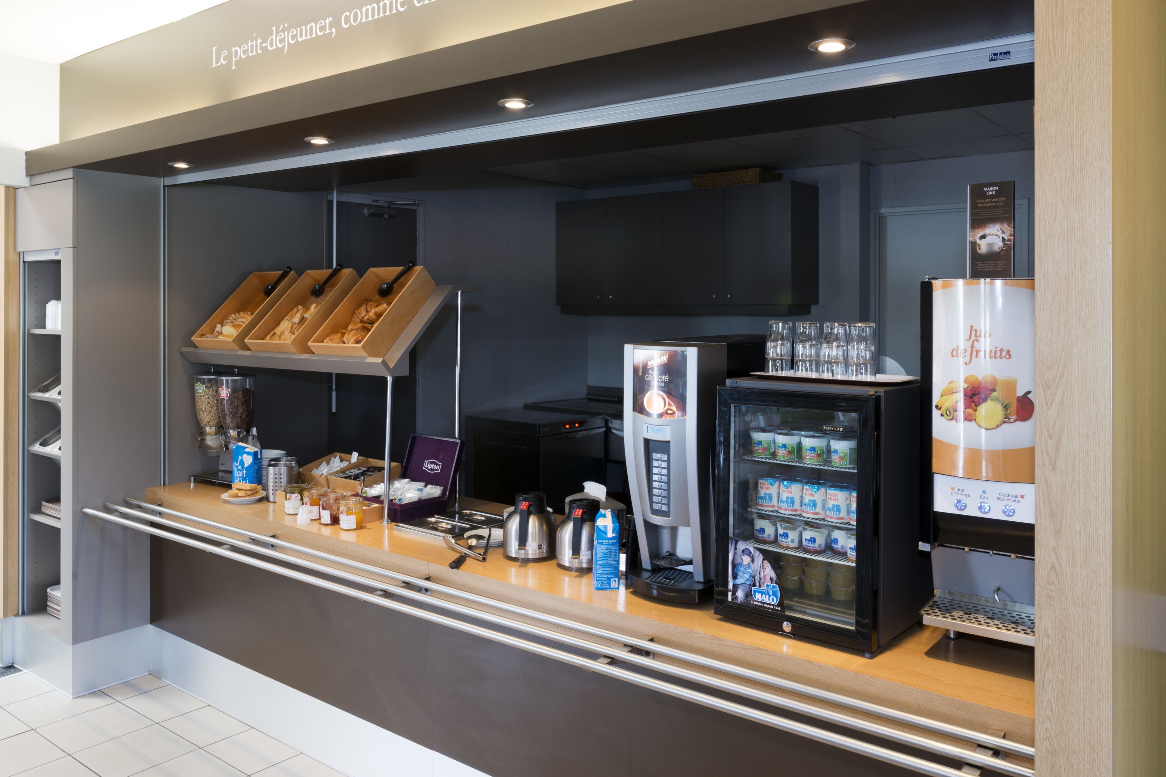 Un espace de petit-déjeuner en libre-service comprenant une machine à café, un présentoir réfrigéré et une variété d’aliments.