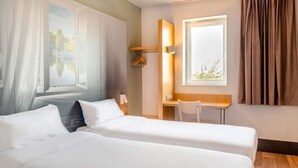 Une chambre d’hôtel avec deux lits, un bureau, une chaise, une fenêtre avec des rideaux et un tableau au mur.