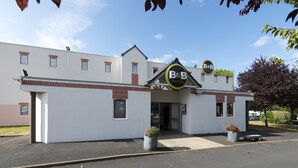 Un hôtel de type « bed and breakfast » avec une façade blanche, un logo bien visible indiquant qu’il s’agit d’un établissement proposant des nuitées et des petits déjeuners, et un parking.