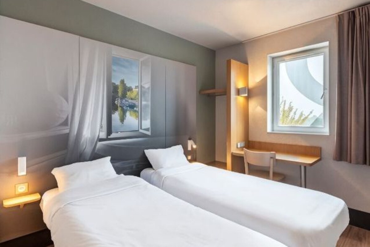 Een hotelkamer met twee enkele bedden, een bureau en een raam met gordijnen.
