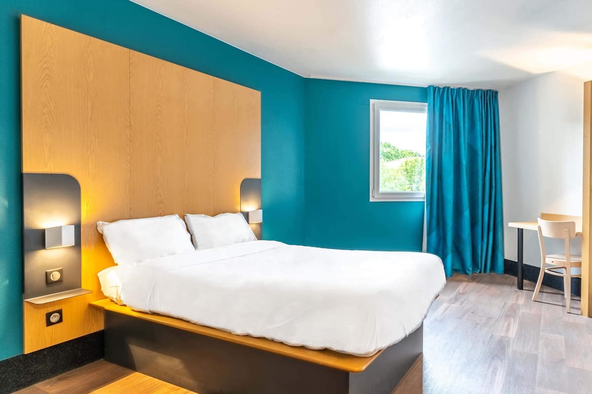 Een moderne hotelkamer met een groot bed, een houten hoofdbord en een klein bureau.