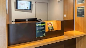 A reception desk with a digital welcome screen, a phone, and informational posters. - B&B HOTEL Aix-en-Provence Le Tholonet (Le Tholonet)
