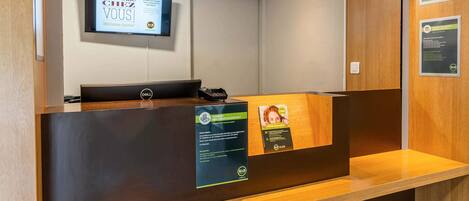 Un mostrador de recepción con una pantalla digital de bienvenida, un teléfono y carteles informativos.
