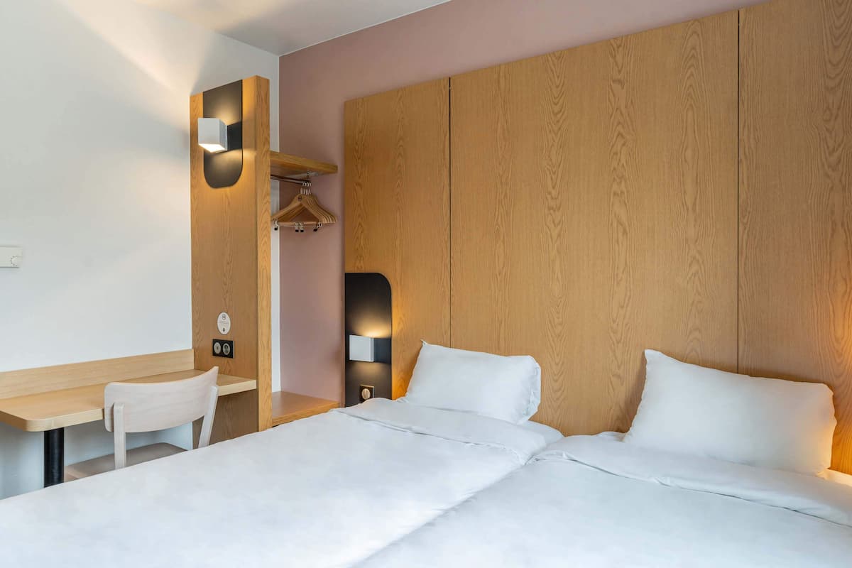 Een hotelkamer met een houten hoofdeinde, een bureau met stoel en een bed met wit beddengoed.