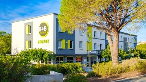 A modern hotel with a prominent B&B logo, a large tree in front, and a well-maintained garden.