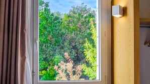 A window with a view of dense foliage, a wooden wall, and a white light fixture.