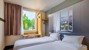 A bedroom with two beds, a desk, and a window with a view of a mountainous landscape.