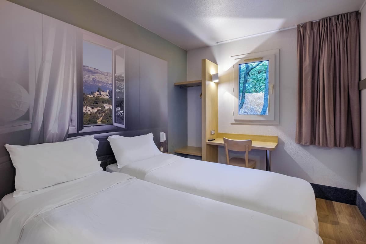 A hotel room with two beds, a desk, and a window with a view of a mountain.