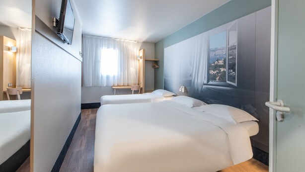 Habitación de hotel con dos camas, un televisor montado en la pared, una ventana con vistas a un paisaje montañoso y suelo de madera.