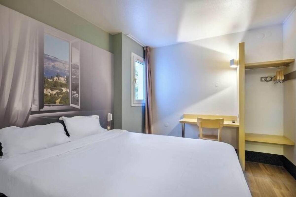 A hotel room with a bed, a desk, a chair, and a wardrobe.