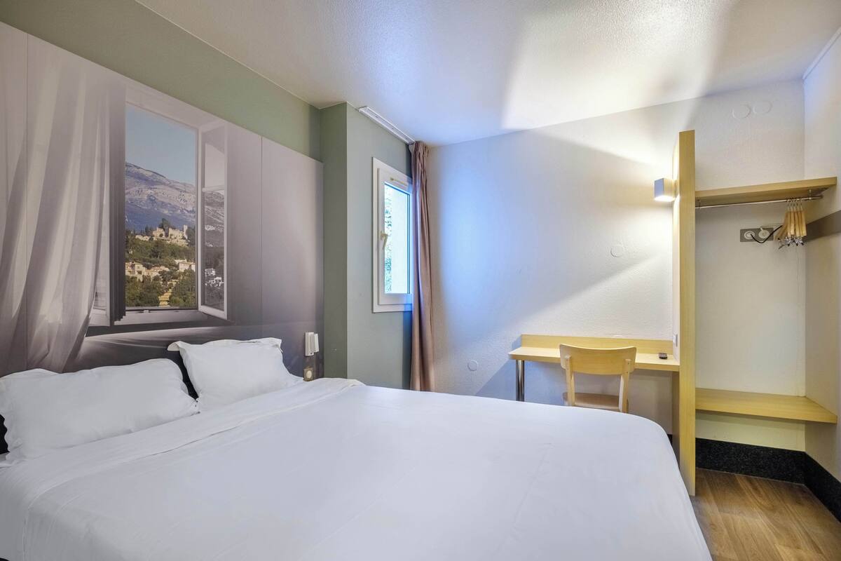 A hotel room with a large bed, a desk, and a view of a mountainous landscape through a window.