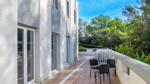 Un edificio moderno con balcón, que incluye una mesa y sillas, rodeado de vegetación.
