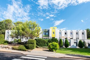 A hotel with a modern design, featuring a prominent 'HOTEL' sign, a well-maintained lawn, and a clear sky. - B&B HOTEL Antibes Sophia Le Relais (Biot)