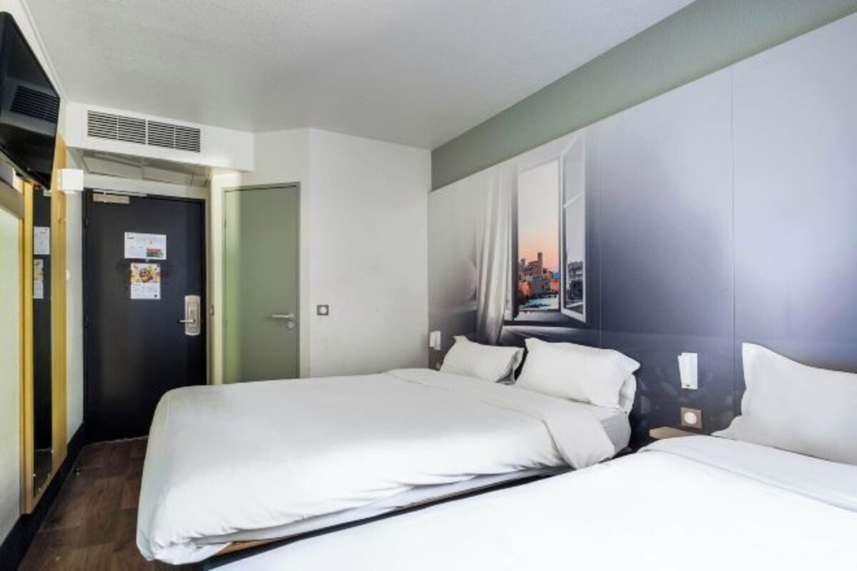 Habitación de hotel con dos camas, una puerta, un aire acondicionado instalado en la pared y una pintura con vista a la ciudad.
