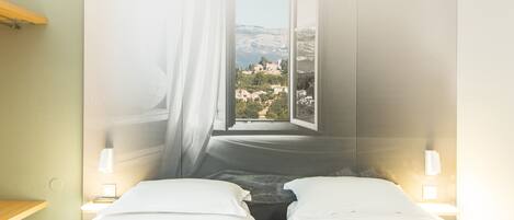 A hotel room with two beds, a window with a view of a mountainous landscape, and bedside lamps.