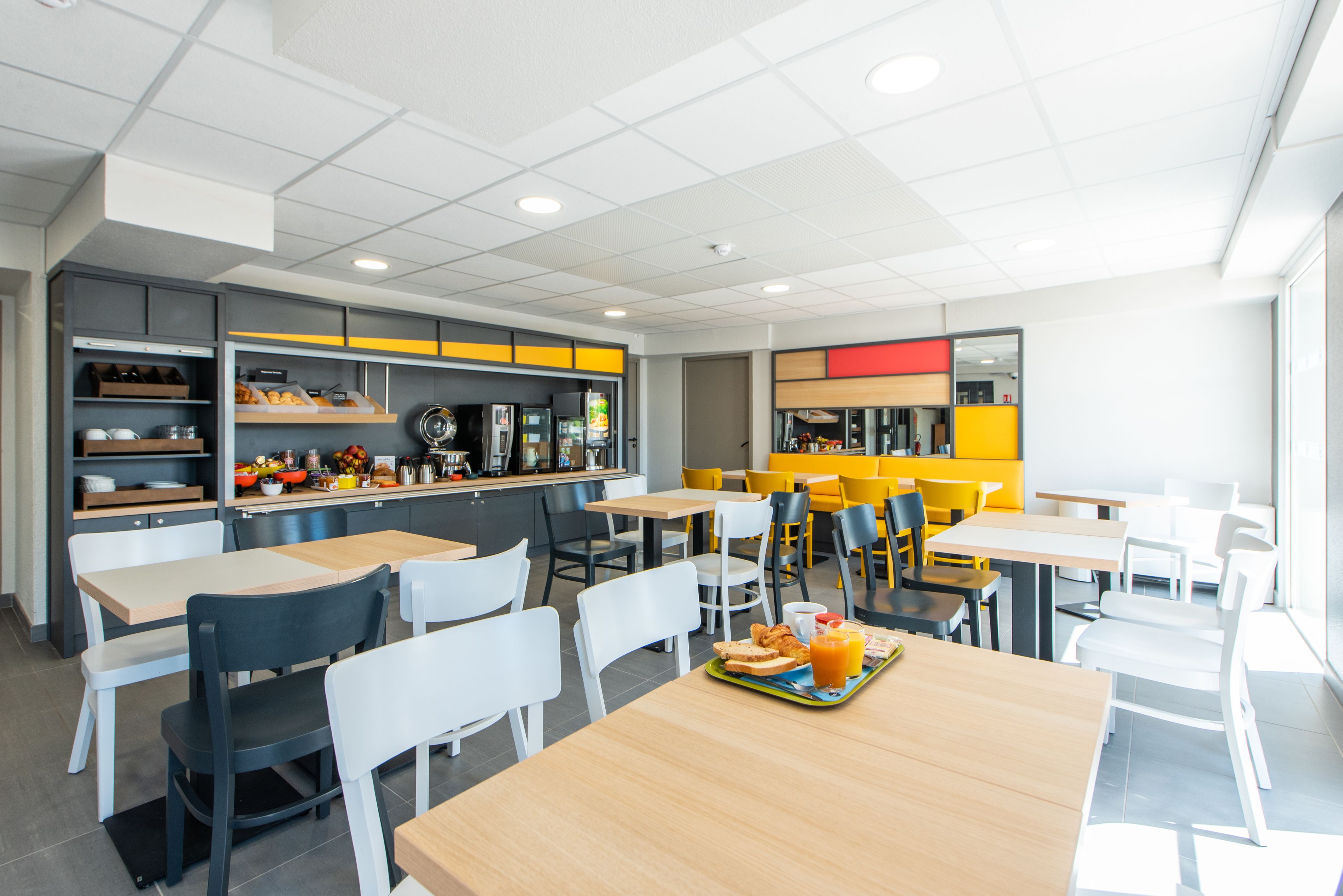 A modern cafeteria with multiple tables and chairs, a counter with food items, and a bright interior.