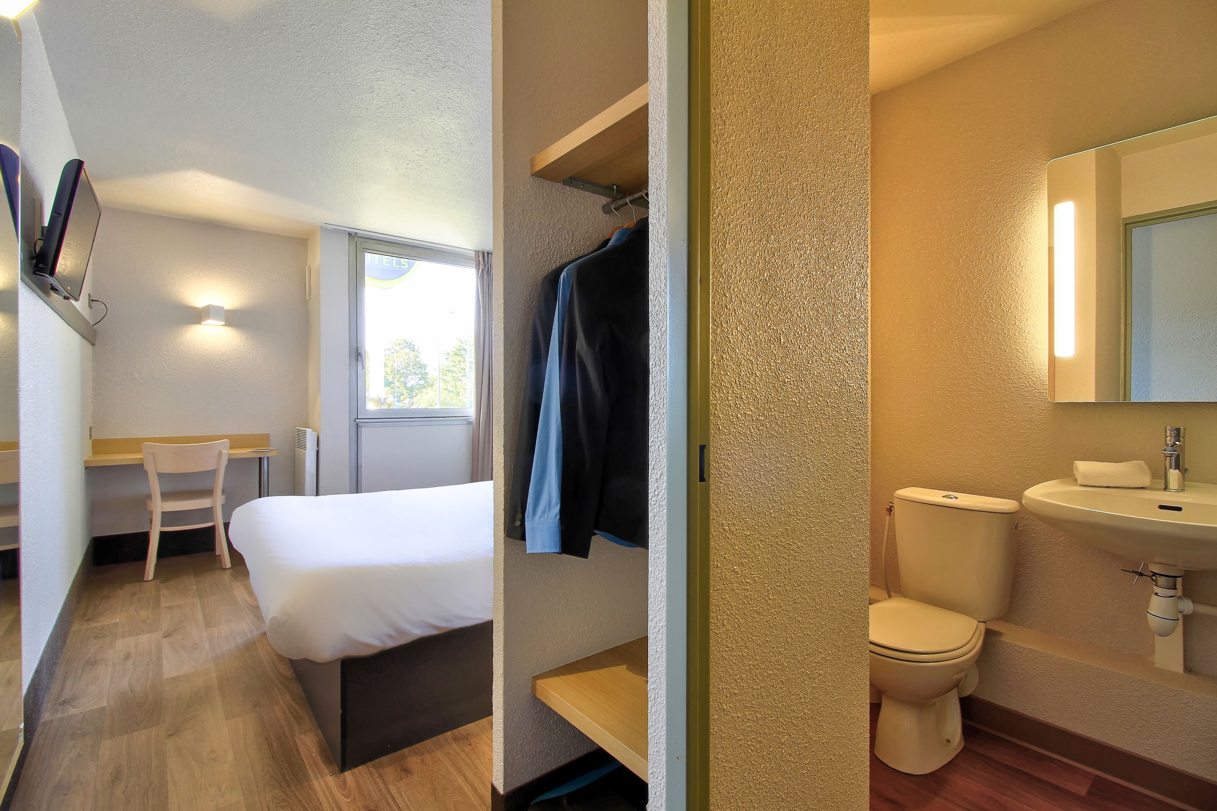 Una habitación de hotel con cama, escritorio, silla, inodoro y lavabo.