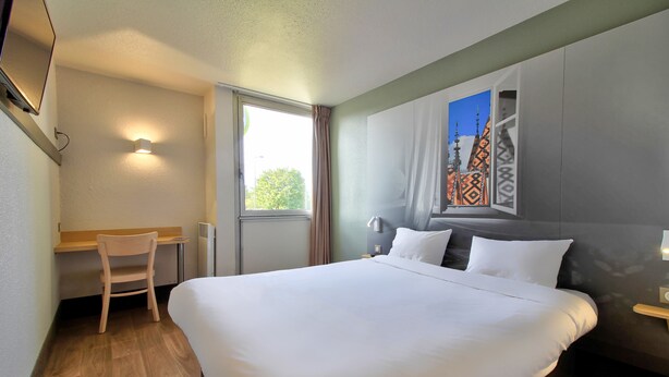 A hotel room with a large bed, a desk, and a window with curtains. - B&B HOTEL Beaune Sud (1) Palais des Congrès (Beaune)