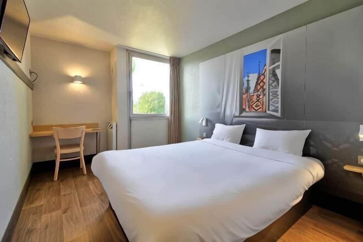 A hotel room with a large bed, a desk, and a chair.