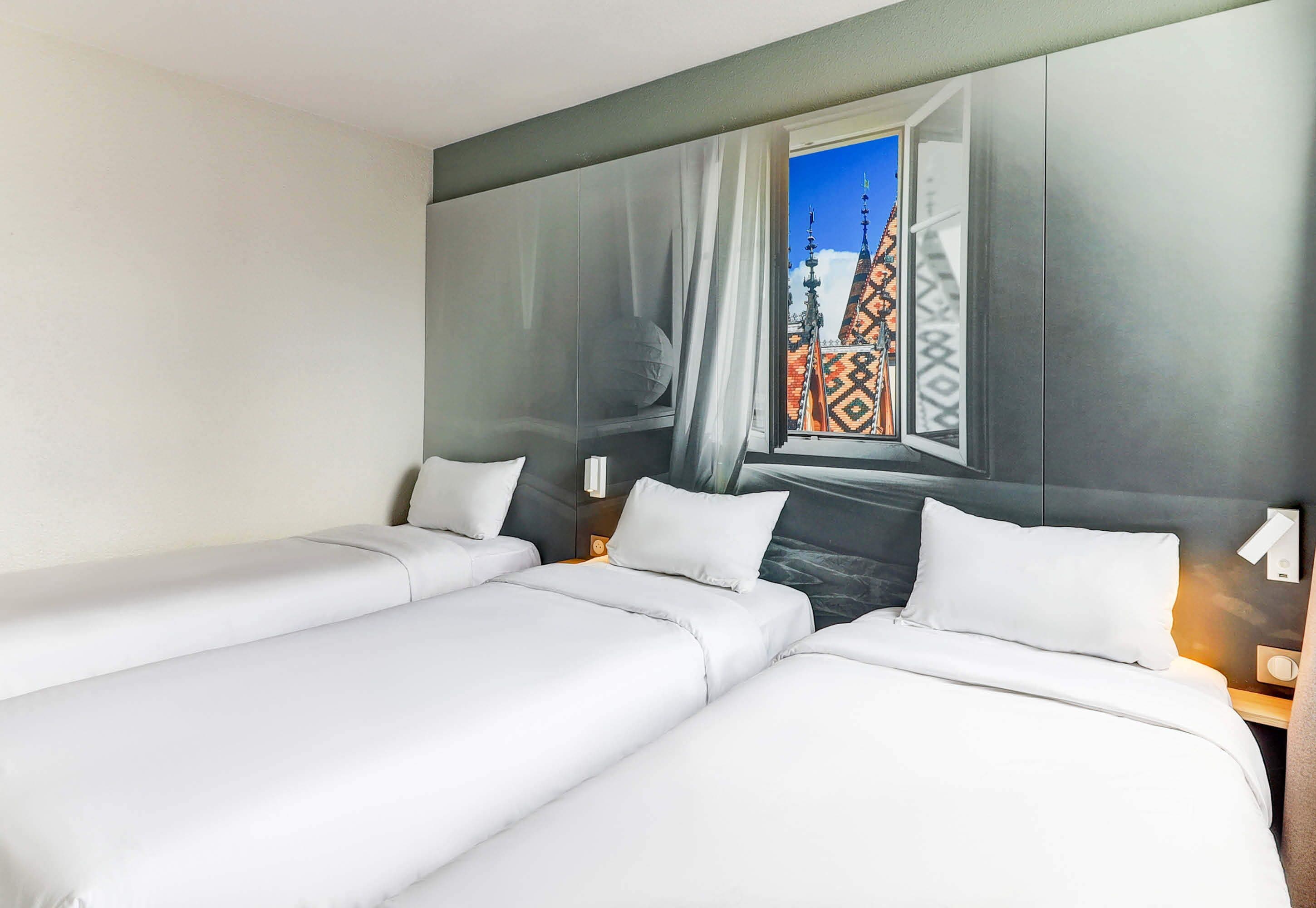 A hotel room with two beds, a large window with a view of a building, and a wall-mounted artwork.