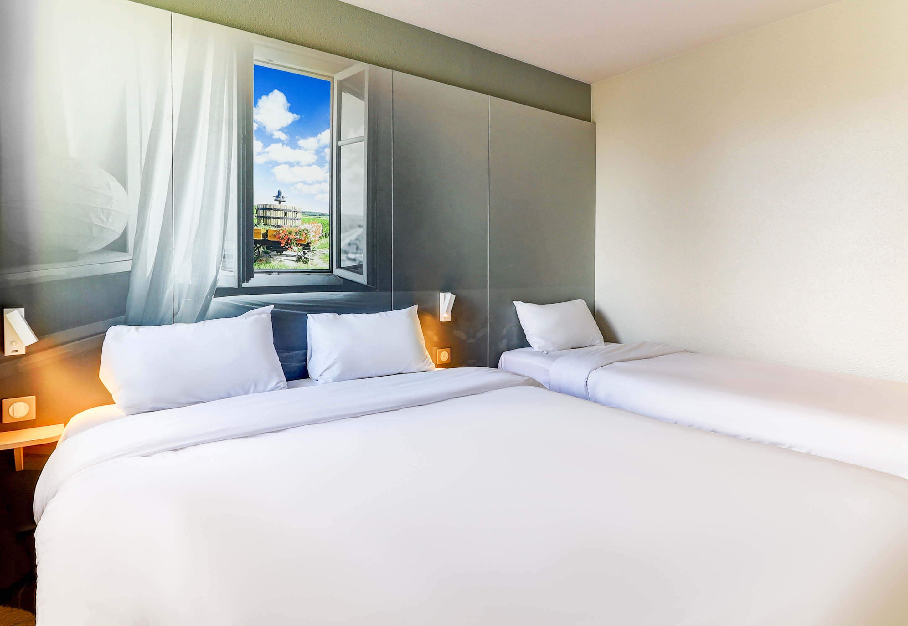 A hotel room with a large bed, a window with curtains, and a view of a garden.