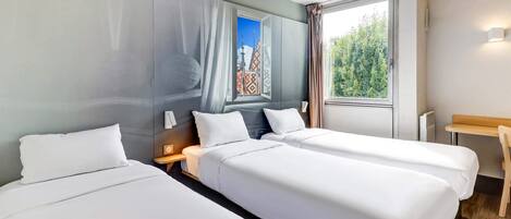 Habitación de hotel con dos camas, un escritorio y una ventana con vista a árboles.