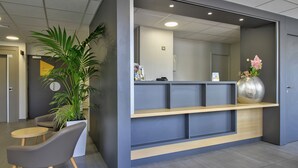A reception area with a desk, chairs, a potted plant, and a decorative vase. - B&B HOTEL Beaune Sud (1) Palais des Congrès (Beaune)
