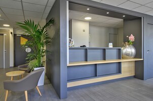 Un área de recepción con un mostrador, sillas, una planta en maceta y un jarrón decorativo.