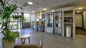 A modern indoor space with a seating area, vending machines, and a microwave. - B&B HOTEL Beaune Sud (1) Palais des Congrès (Beaune)