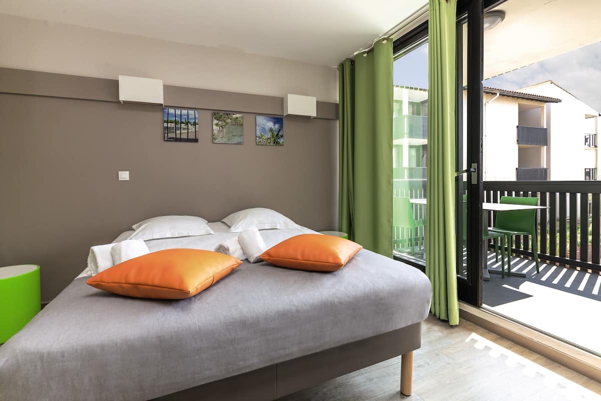 Un dormitorio con cama, almohadas, una mesita de noche y vistas a un balcón exterior.
