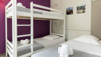 Une chambre avec un lit superposé, un mur violet, un lit blanc et deux petits tableaux accrochés au mur.