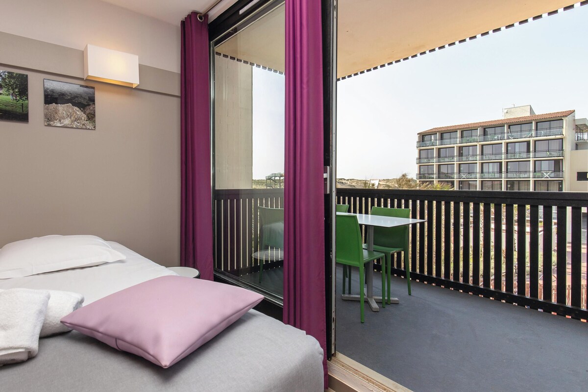 Habitación de hotel con cama, ventana con cortinas, mesa con sillas y vista del edificio exterior.