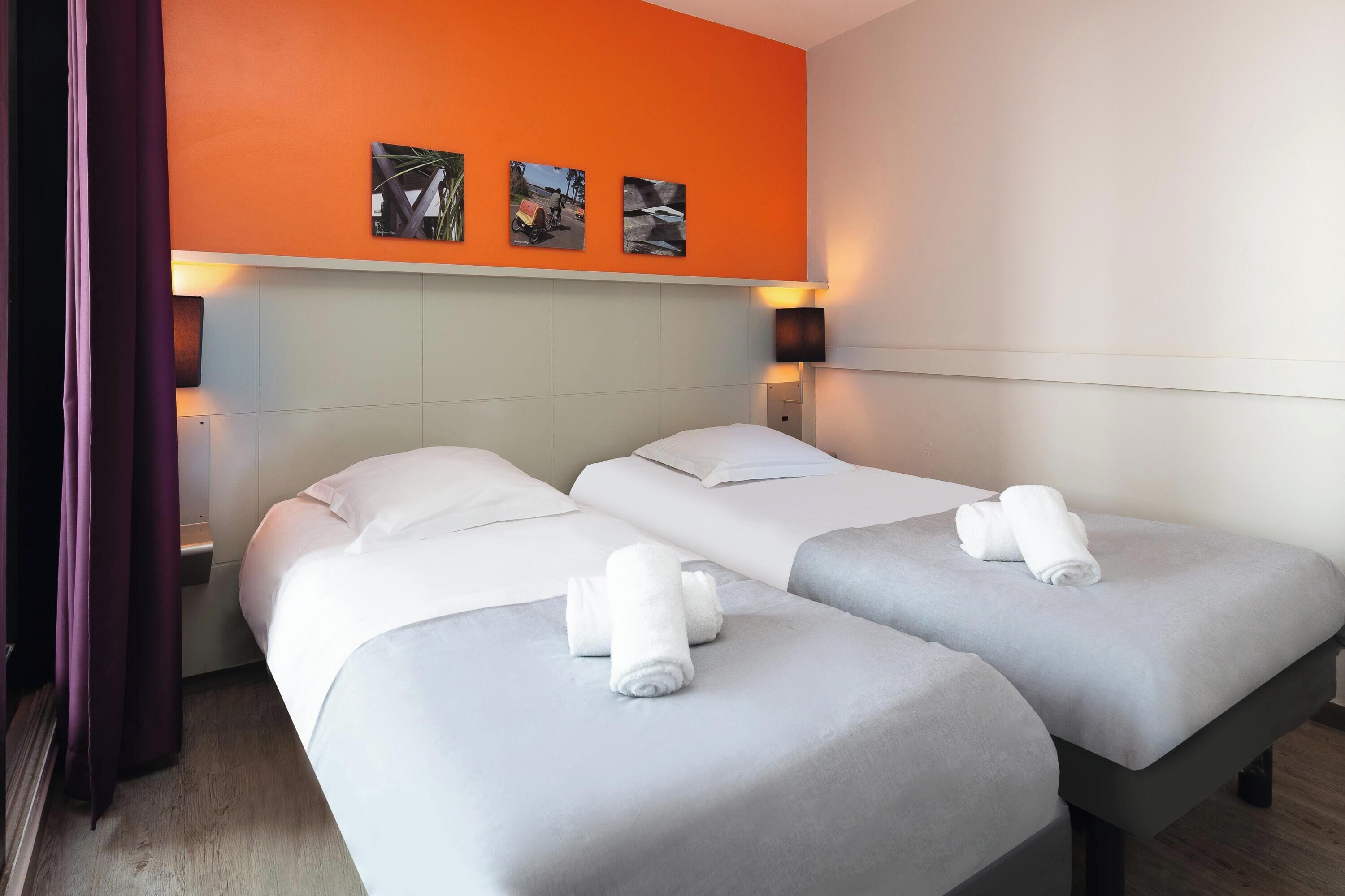 Une chambre d’hôtel avec deux lits, une tête de lit, des lampes fixées au mur et des œuvres d’art.