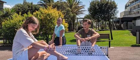 A table tennis table outdoors with a few people around it.