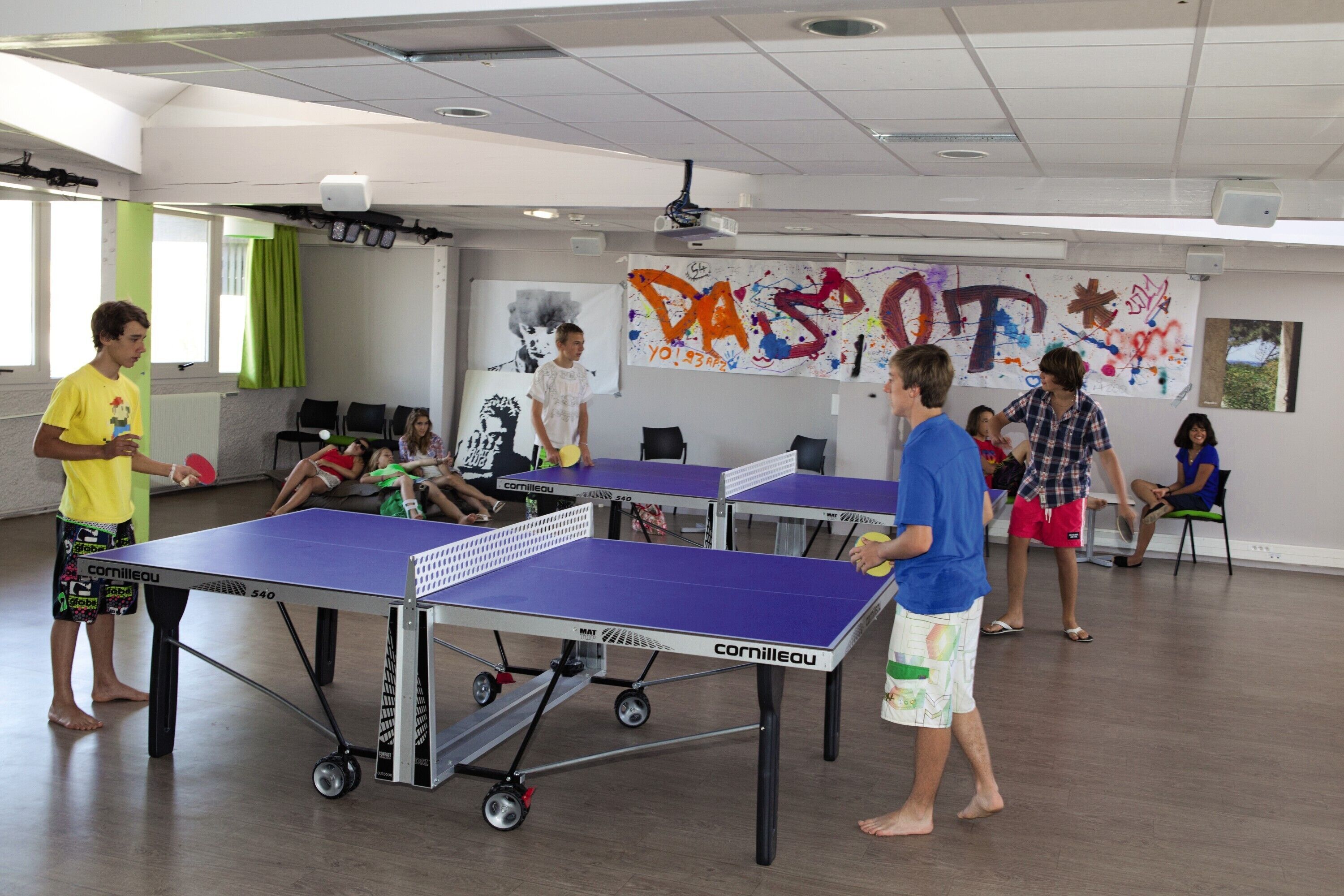 A room with ping pong tables, a projector, and a wall with colorful graffiti.